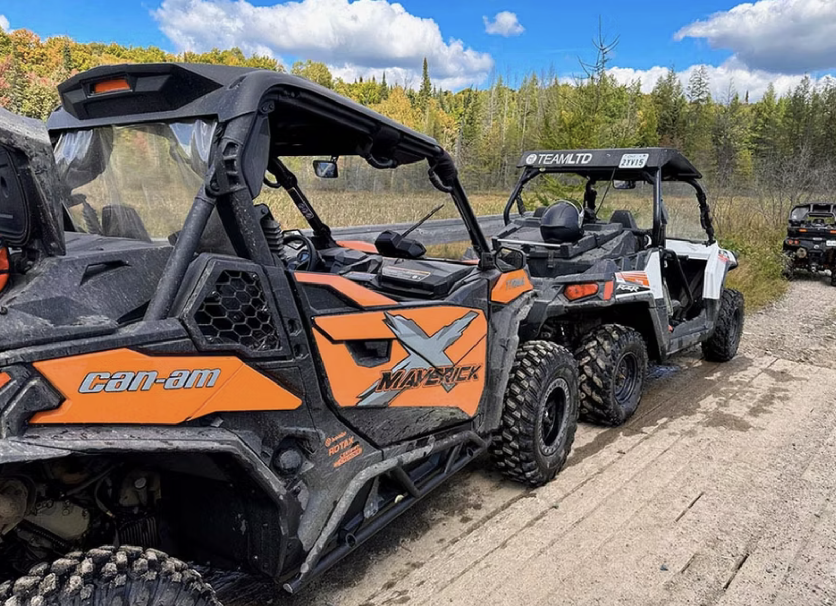 A row of UTVs parked by the side of a wooden bridge along forested trail in the late summer.