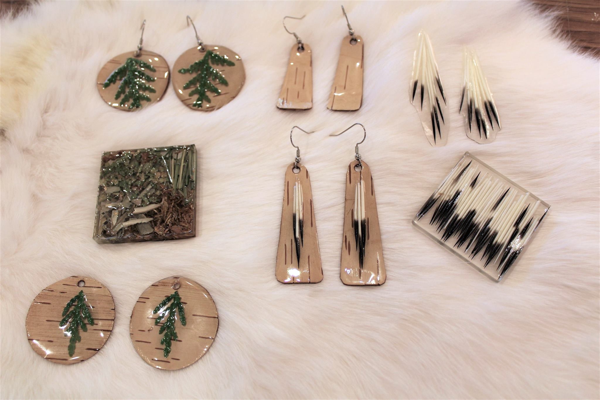 resin and wood earrings laid out on a white fur—each is decorated with a different pattern of black and white porcupine quill or cedar sprig.