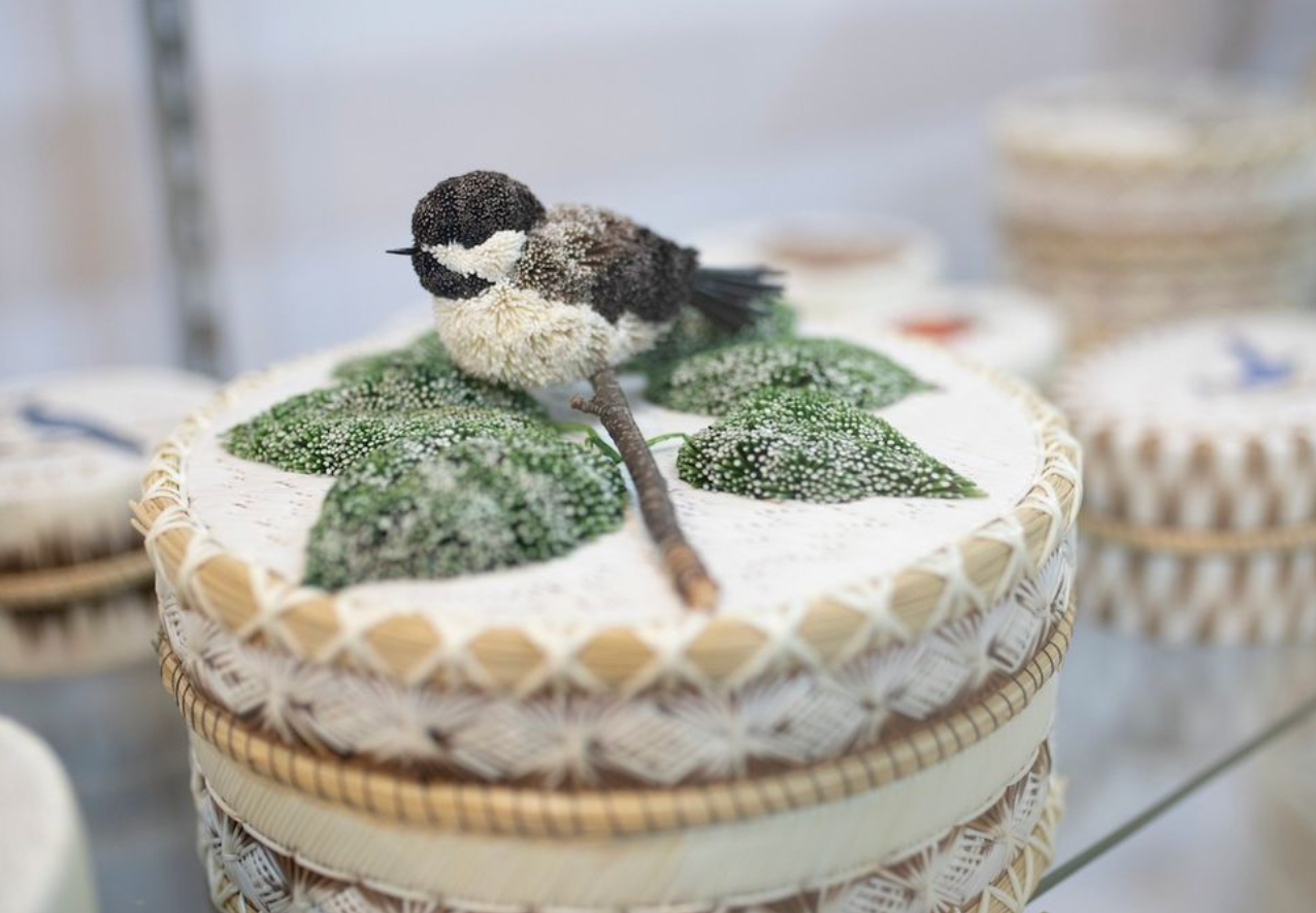 A handcrafted round wooden box finely decorated with a 3-dimensional chickadee and leaf motif made out of coloured porcupine quills.