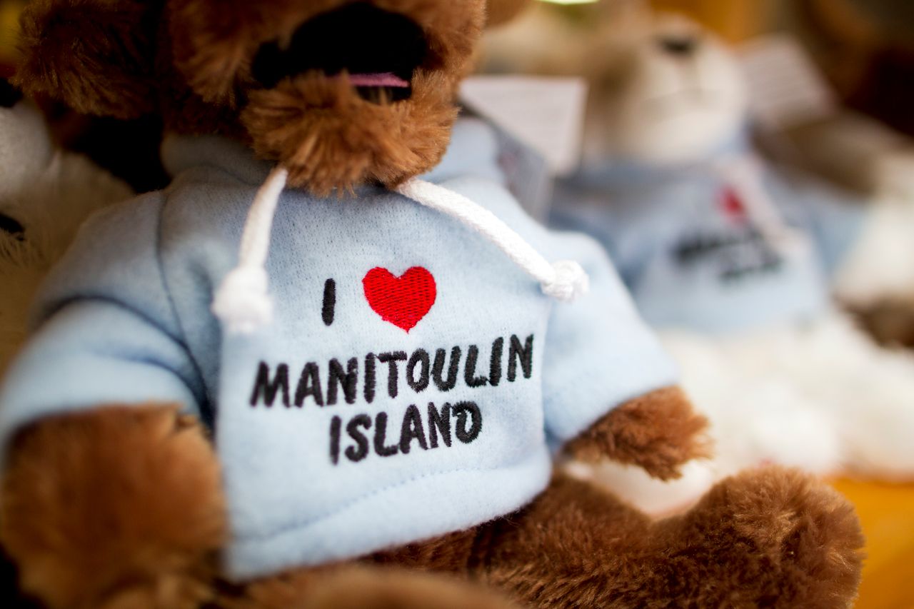 a row of teddy bears wearing little white t-shirts embroidered with an "I love Manitoulin Island" emblem.