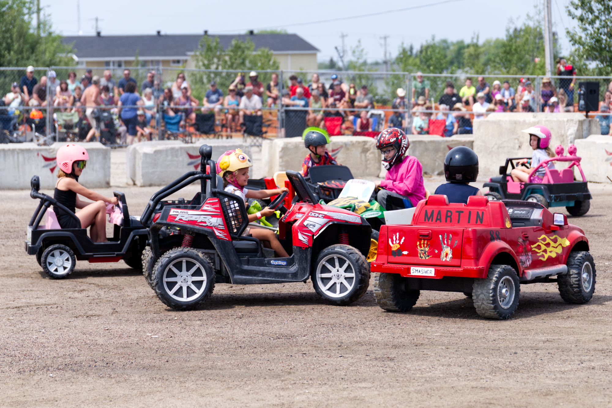 children driving powerwheels cars drive around a dirt ring at the fairgrounds, holding their own mini-derby.