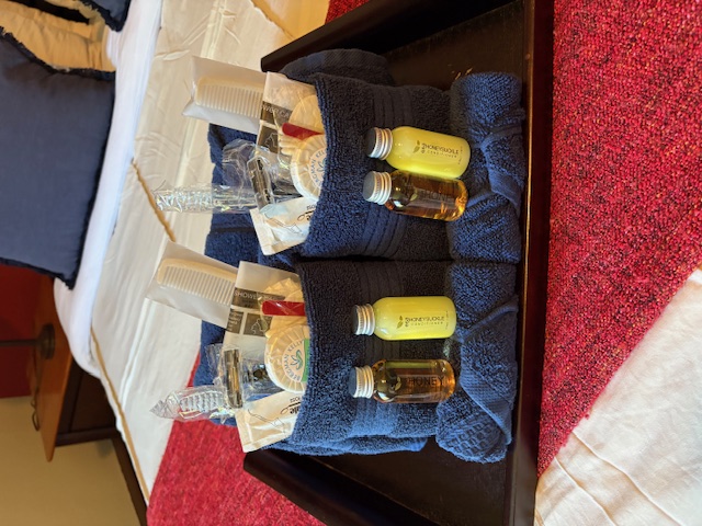 two sets of soaps and toiletries elegantly wrapped in luxurious dark blue towels and laid out on a crisply made bed.
