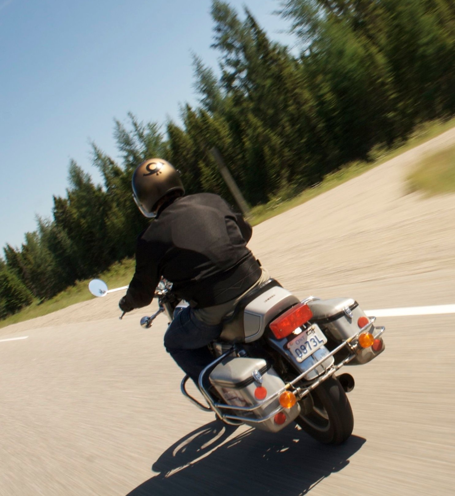 A motorcyclist riding along Highway 11 in the summer—an empty highway surrounded by thick boreal forest.