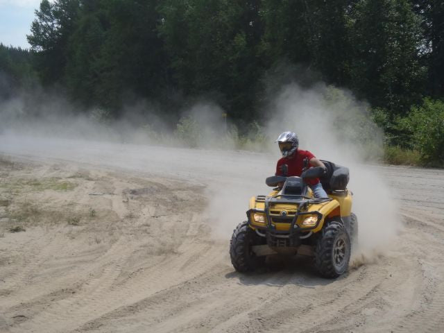 An ATV rider raises a large cloud of dust while zooming around a turn on a forest trail.