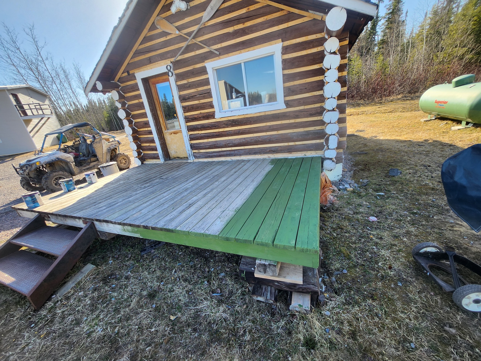 a tidy log cabin with wooden canoe paddles crossed over the door and a green wooden plank porch. 