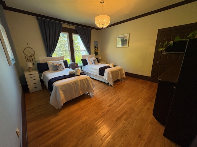 a set of twin beds in a stately room with polished wooden floors, a glowing glass chandelier and tall antique windows.