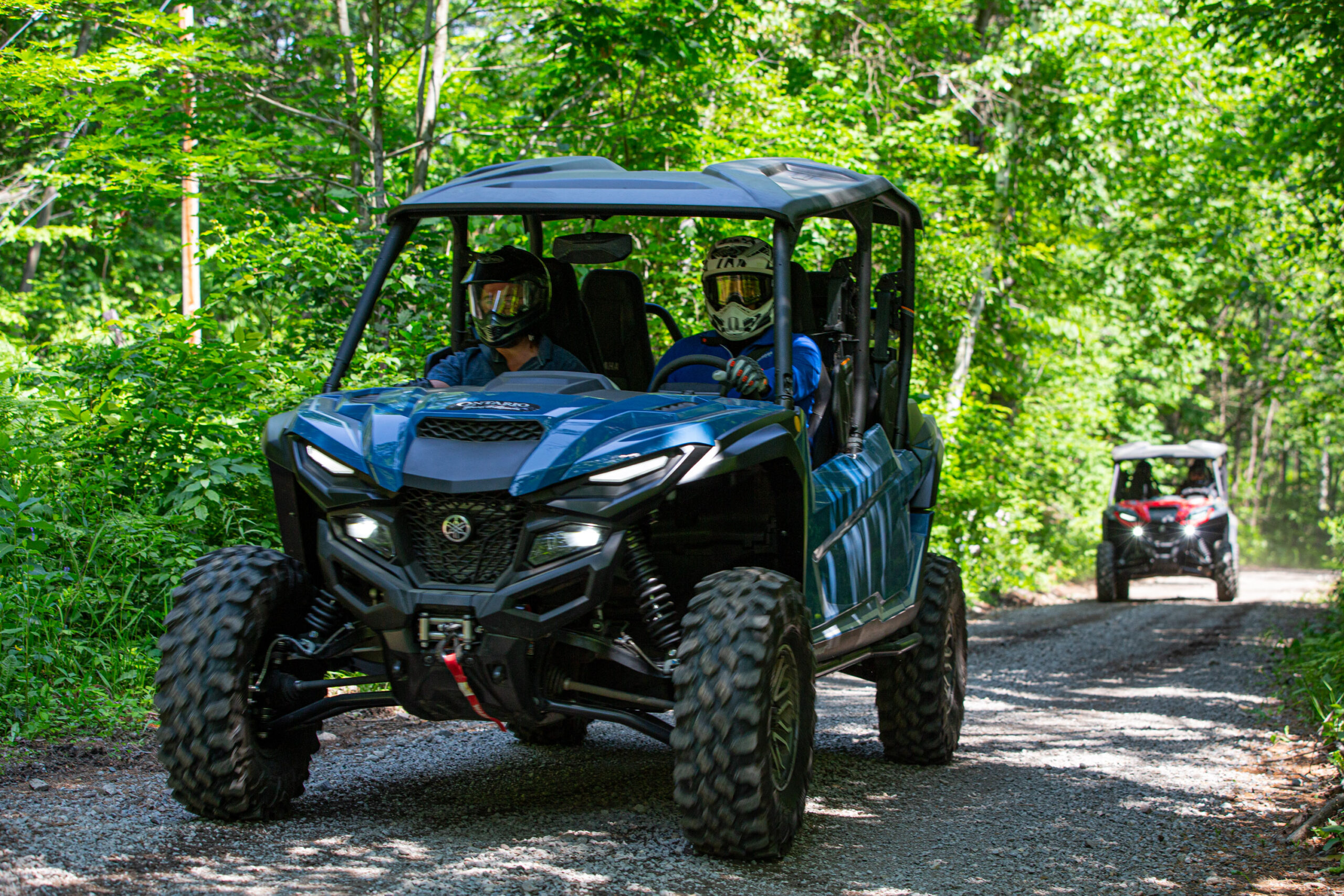two side-by-sides roll down a shady, forested trail on a summer day at the Rockin' the Trail event.