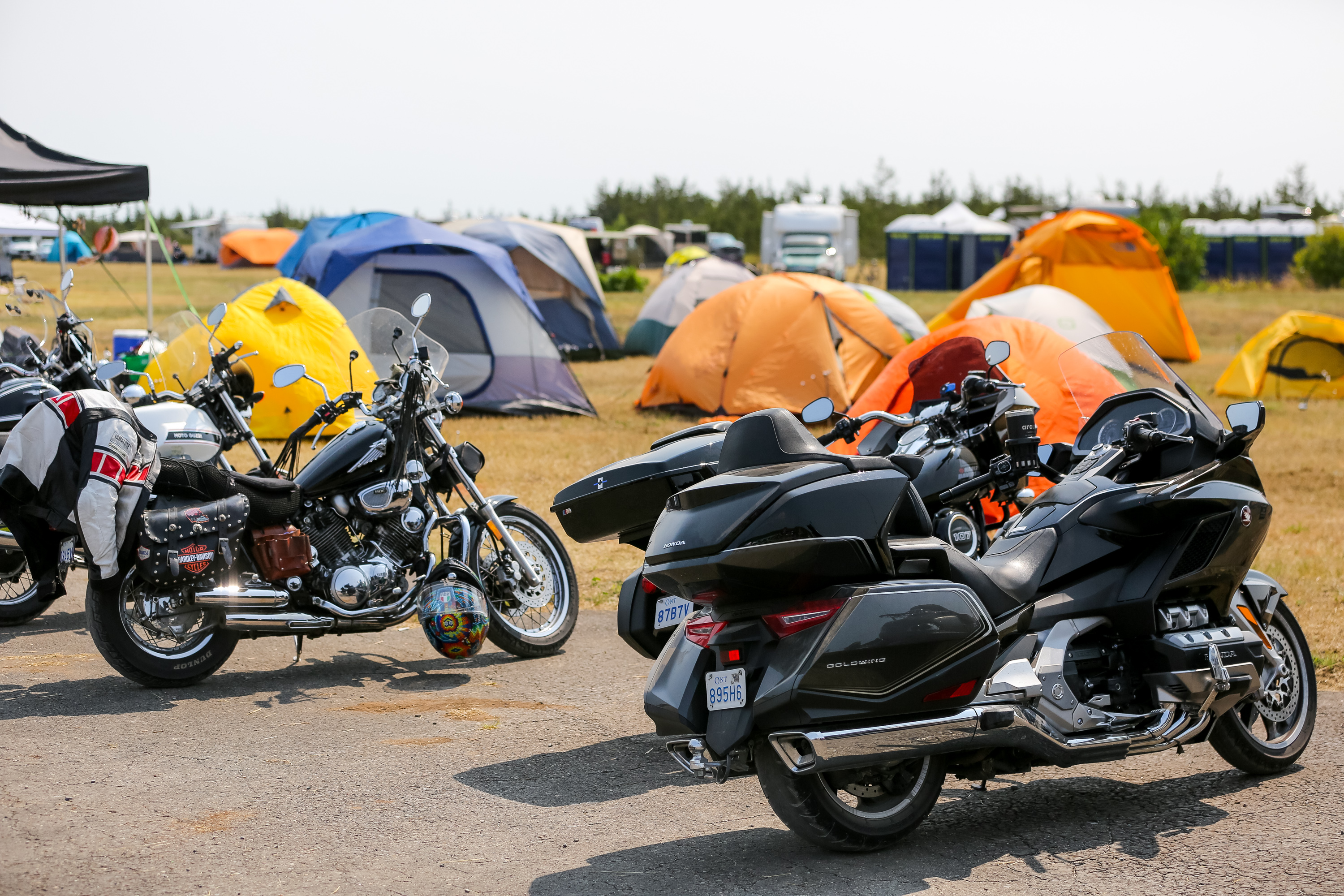 several motorcycles parked next to multiple rows of tents in a green field at Moto Craft in Ontario.
