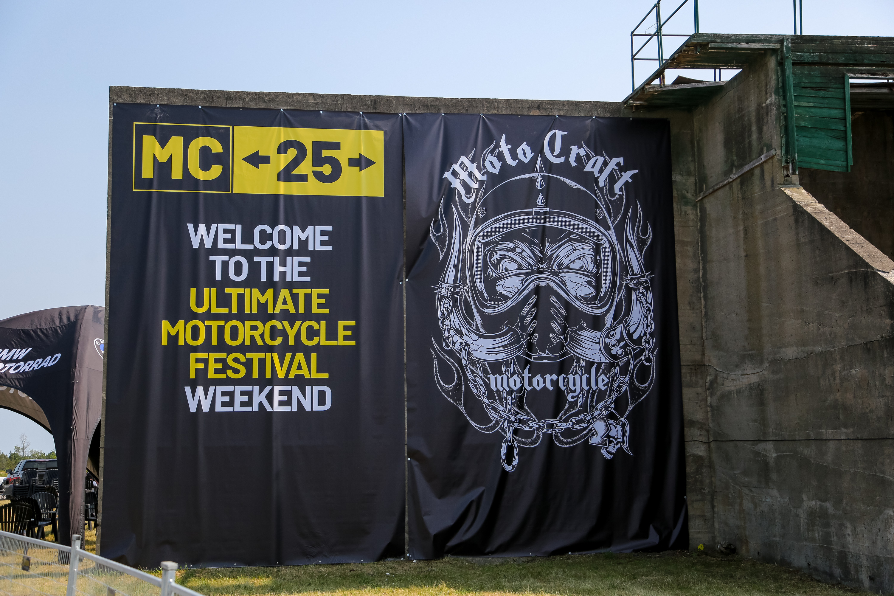 A 3-storey-tall sign for Moto Craft 2025, showing an artistically rendered helmeted face next to the words "Welcome to the Ultimate Motorcycle Festival Weekend!"