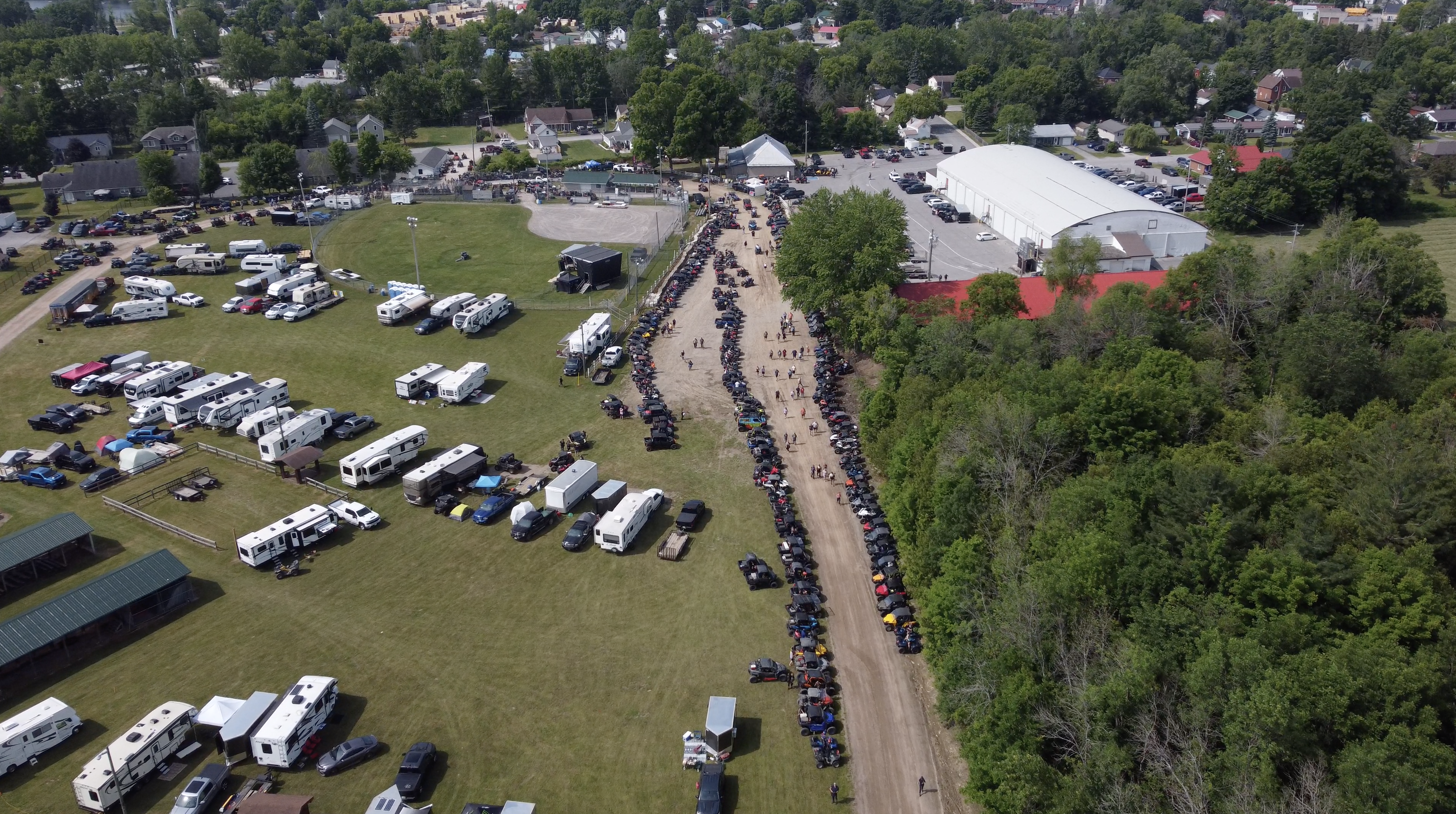 rows of campers parked in the green field next to the Tweed Fairgrounds, with hundreds of ATVs parked along a the long dirt road leading up to the Rockin' the Trails festival grounds.