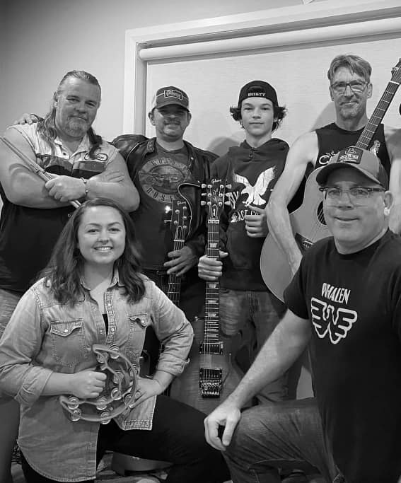 a band of six members smiling and holding their instruments.