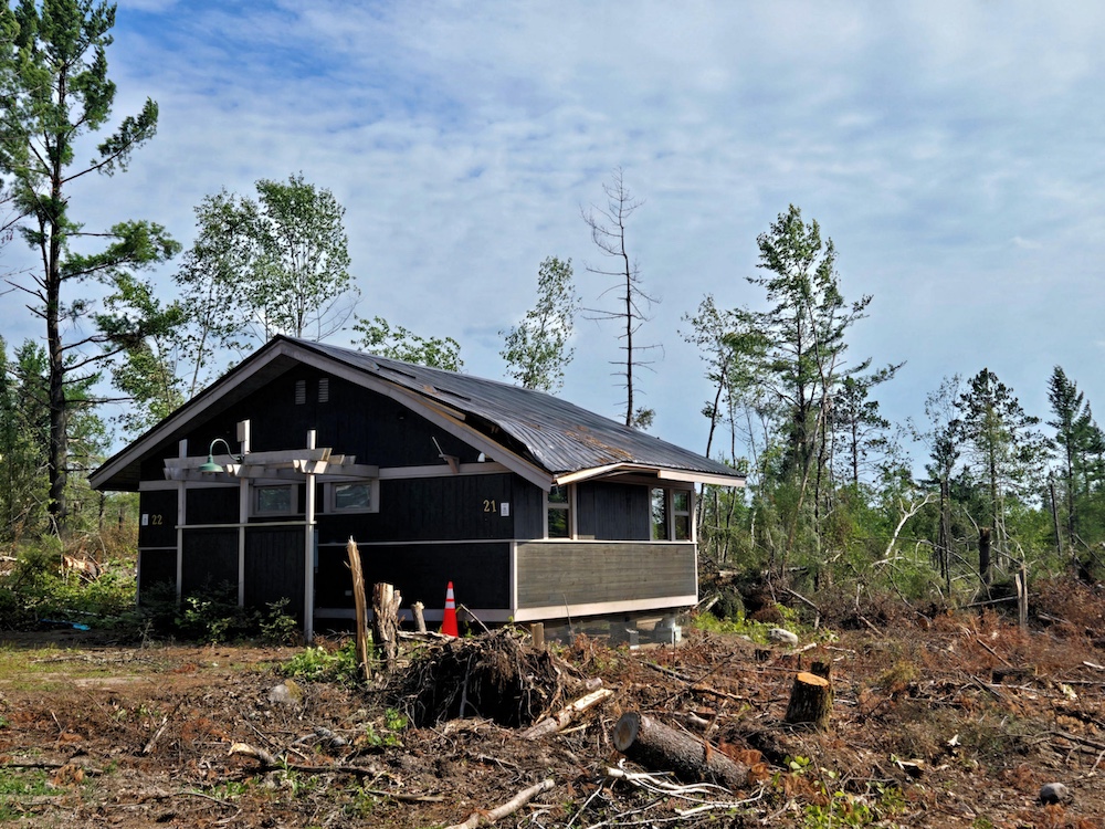 Roof of cabin partly caved in with tree damage all around