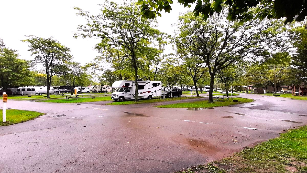 An RV parked at a tidy, paved campground filled with lush green trees.