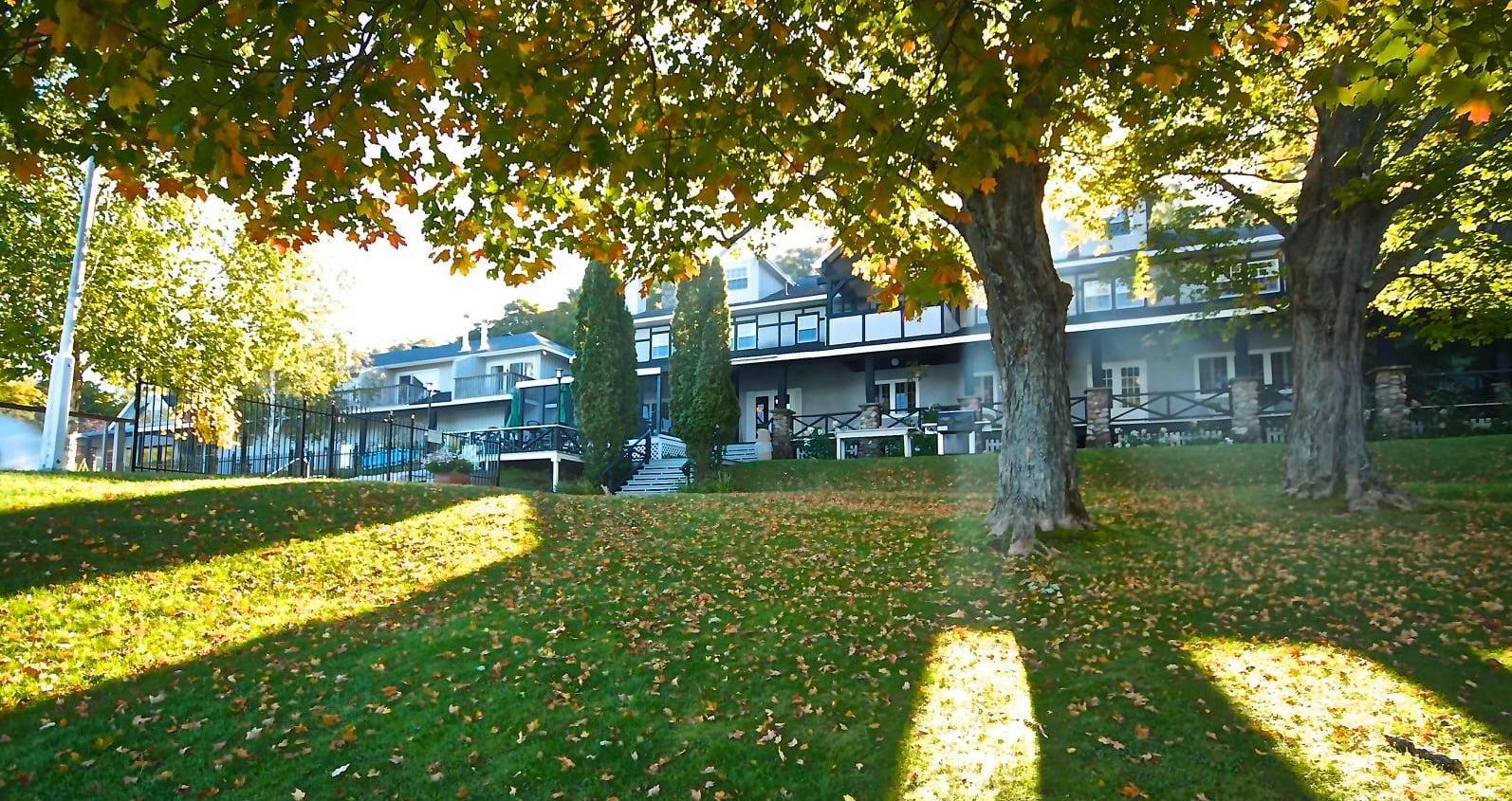 Sir Sam's Inn & Spa; a large, elegant resort building surrounded by rolling green lawn and large, stately shade trees casting late afternoon shadows with leaves turning golden for fall. 