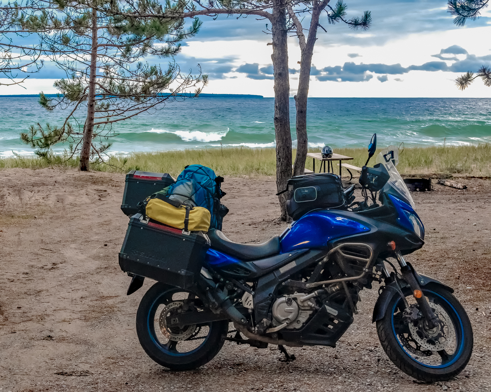 Turquoise waves crash onto Agawa Bay Beach next to a motorcyle parked on the sand under tall pine trees.
