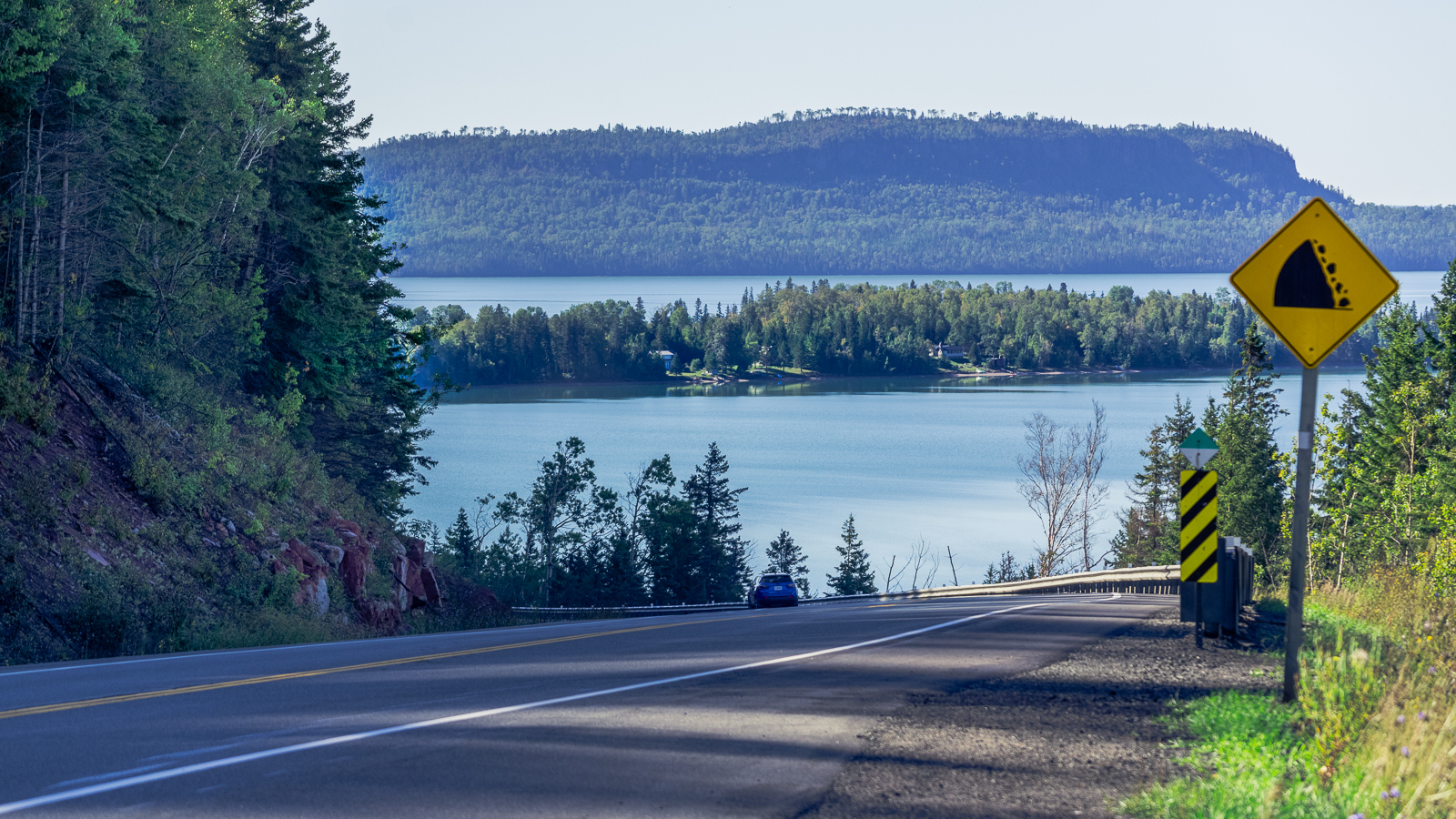 cresting a hill on highway 17 shows the wide, blue Lake Superior below, skirted by untamed forest and rocky banks.