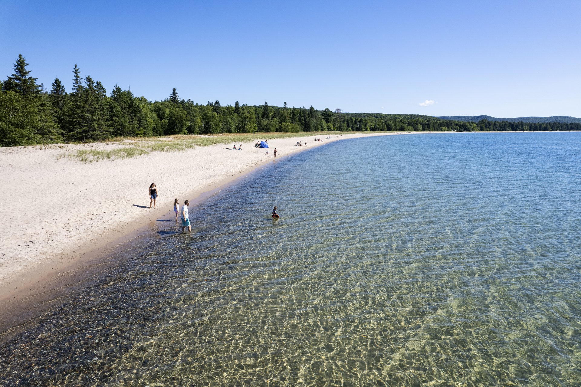 a few people dot a white sand beach that stretches the length of a crystal clear rippling bay on Lake Superior.
