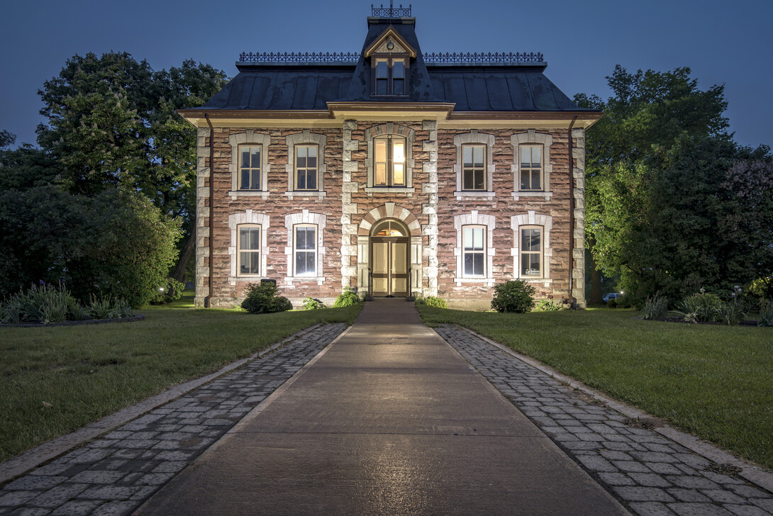 The antique stone Administration Building at the Sault Ste. Marie Canal, looming at dusk with only one lit window on the top floor. 