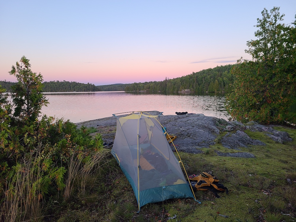 Tent on rocky outcrop next to lake at sunset