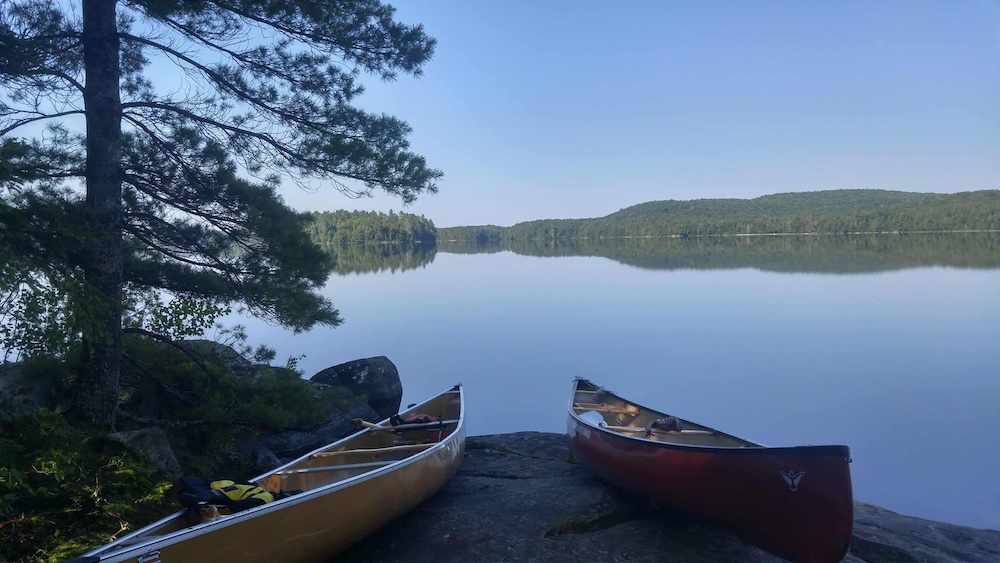 Two canoes sitting on shore with lake in background