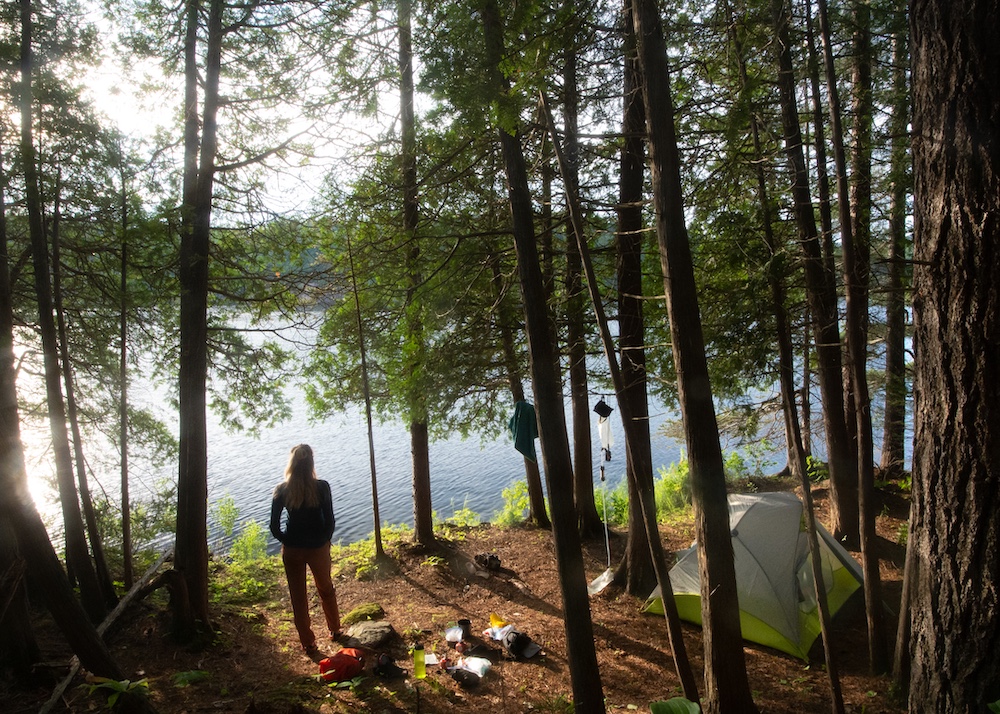 Woman stands on campsite with tent and other gear strewn about