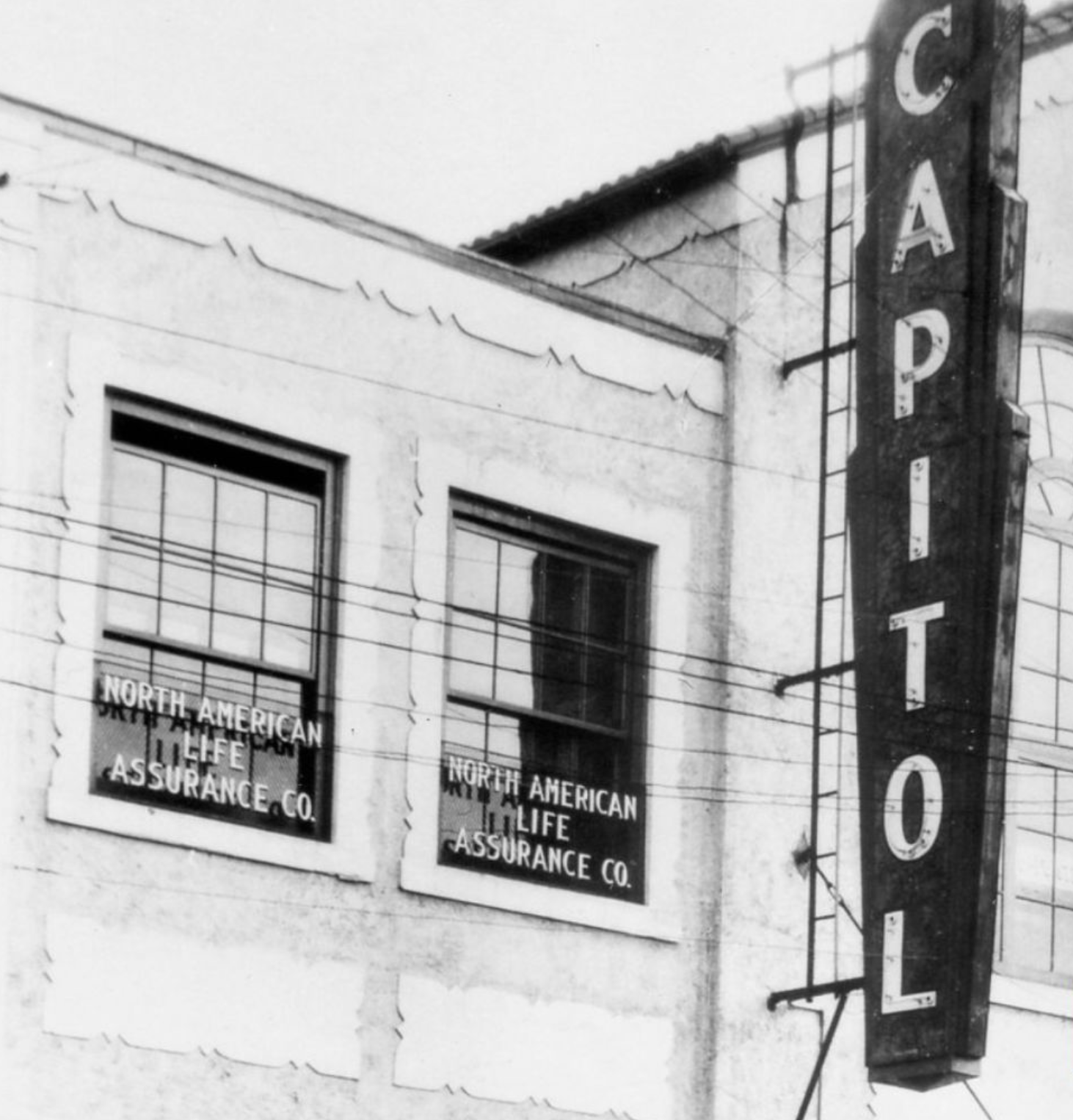 a black and white photograph of the old electric Capitol theatre sign attached to the side of the building next to dark paned windows.