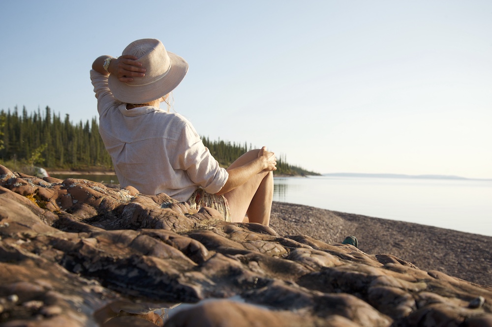Woman sitting on a beach looking out at lake