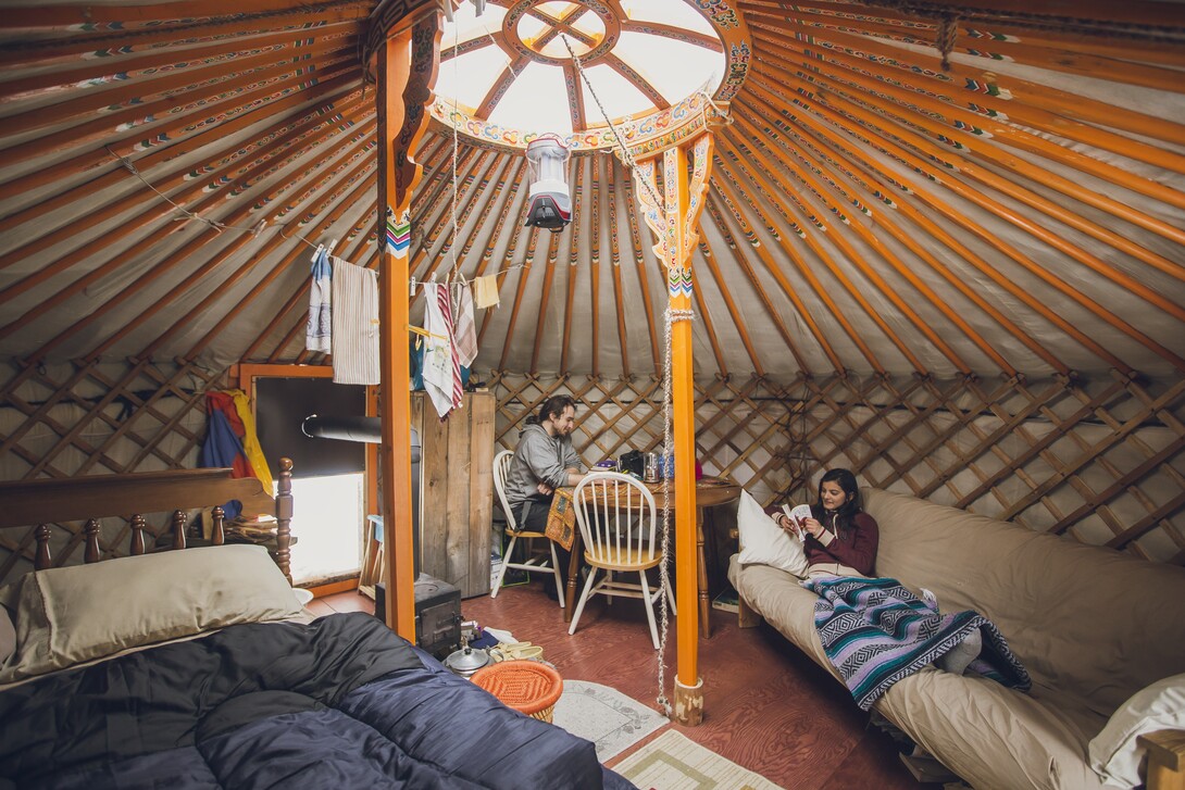 a man and woman lounge in a large, cozy yurt with comfortable beds and couches at Nature's Harmony Ecolodge near North Bay, Ontario.