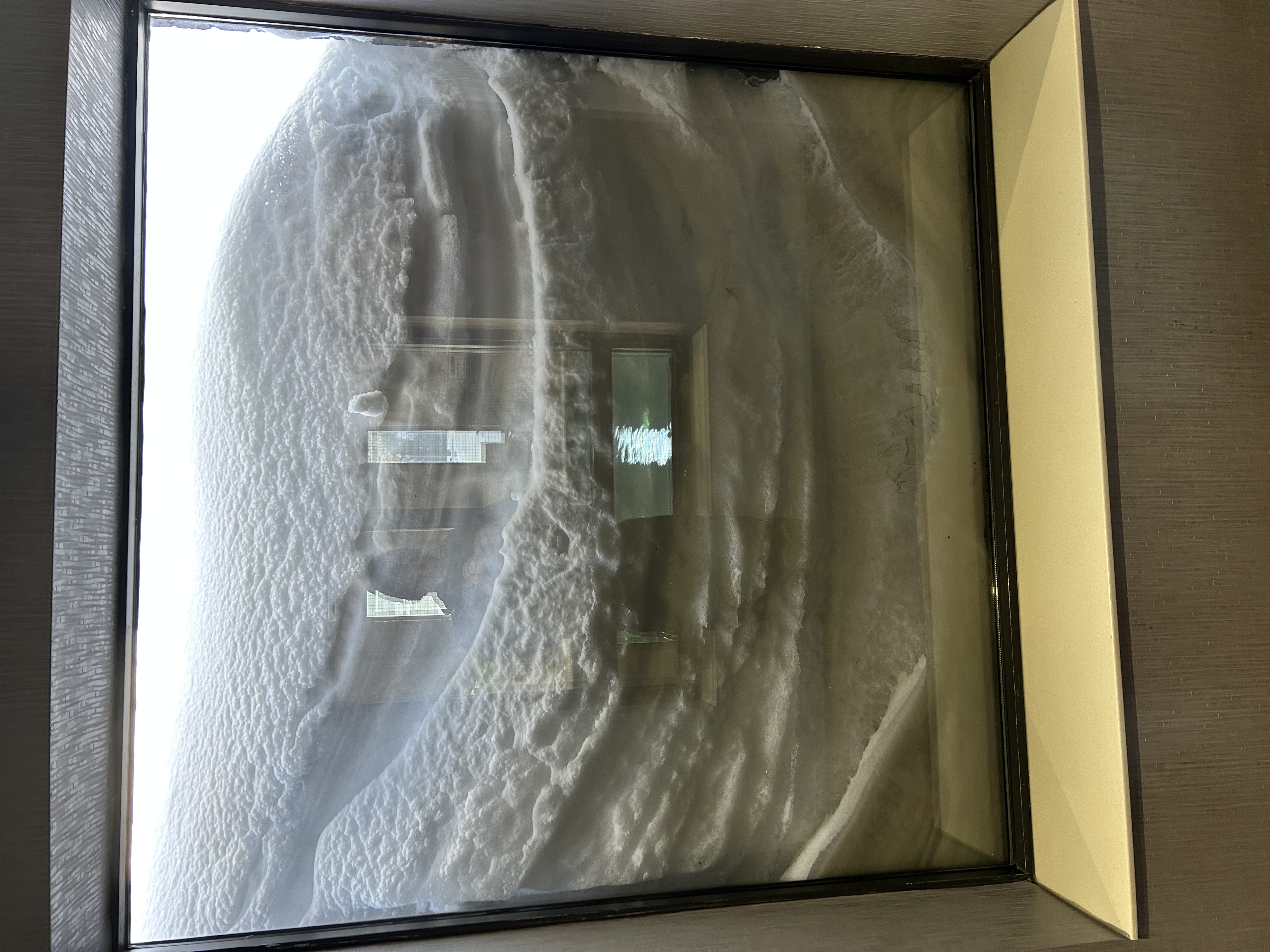 The window at the Quattro Hotel in Sault Ste Marie, with snow built up outside so deep that it covers the window completely except for a small crack of daylight at the top.