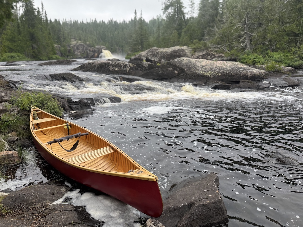Red canoe sits on rocks with waterfall in background