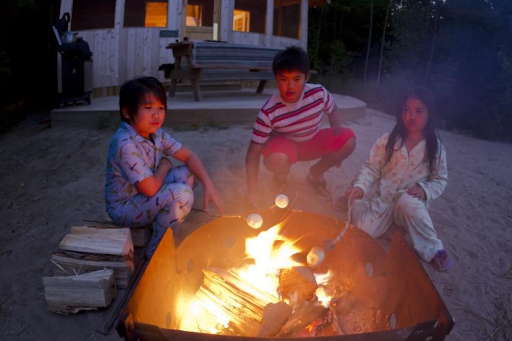 Three kids roasting marshmallows over a campfire