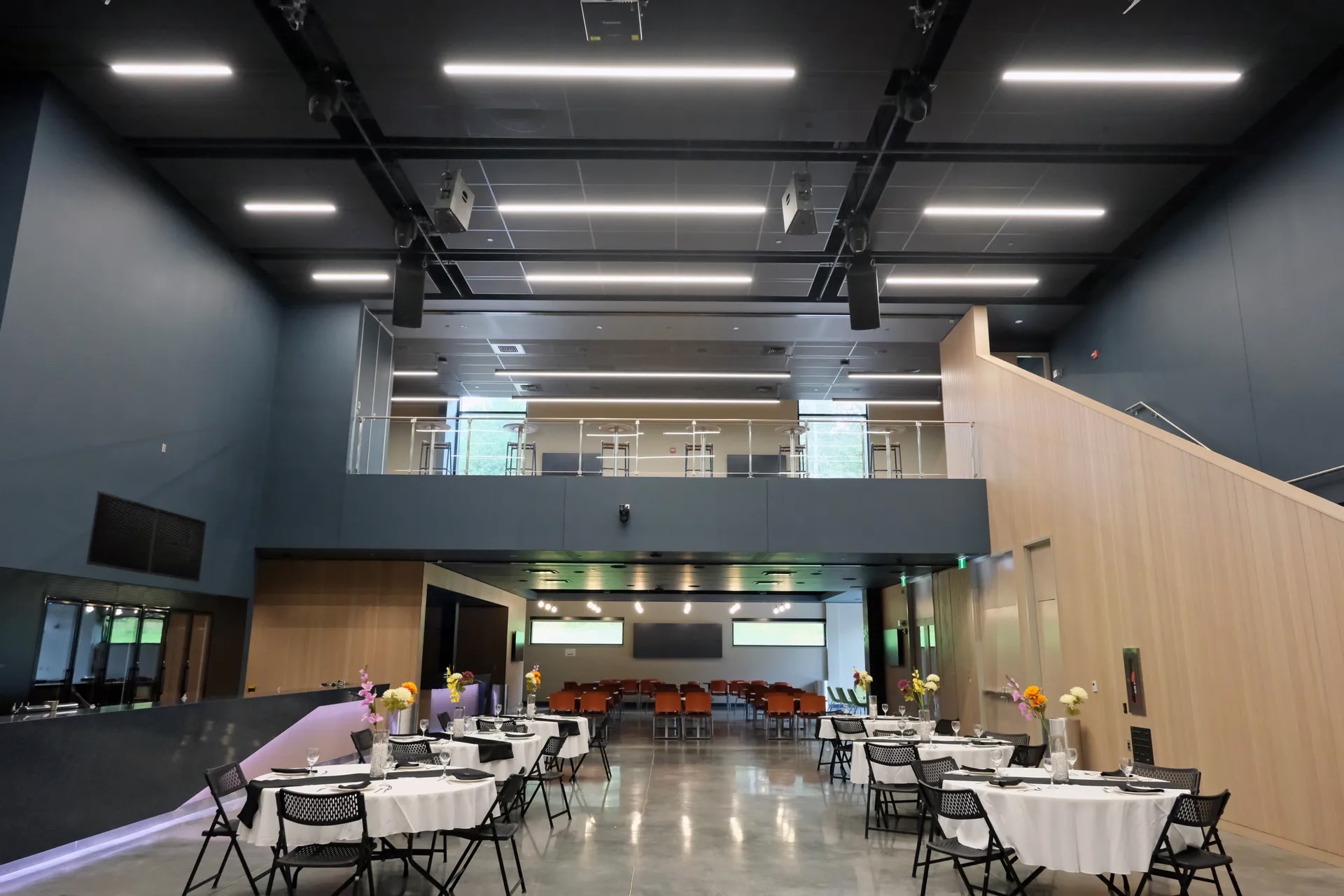 a tall-roofed conference space with tables and chairs, shiny floors and modern lighting.