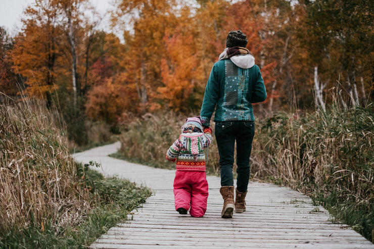 a woman and child wearing winter clothing walk down a wooden boardwalk through a golden autumn forest at Laurier Woods Conservation Area.