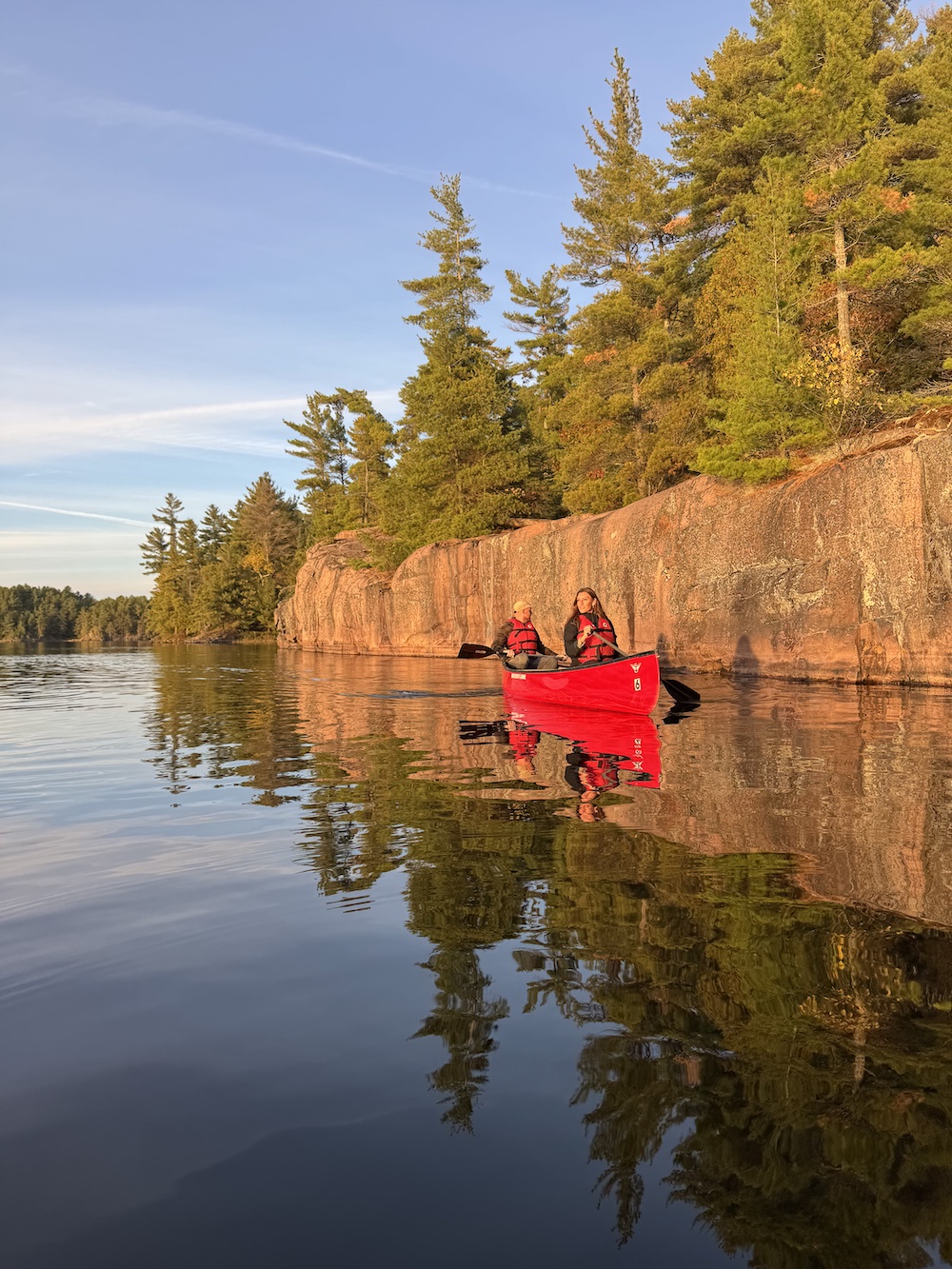 Two people in red canoe paddling beside cliffs on a lake