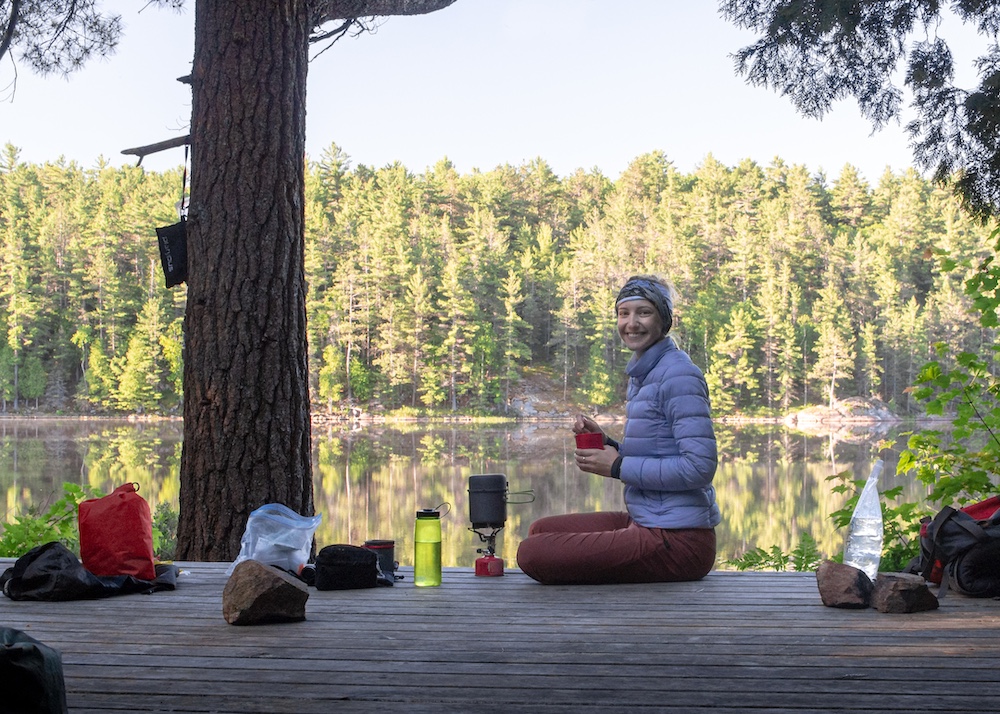 Woman sits on wooden tent platform with lake in background
