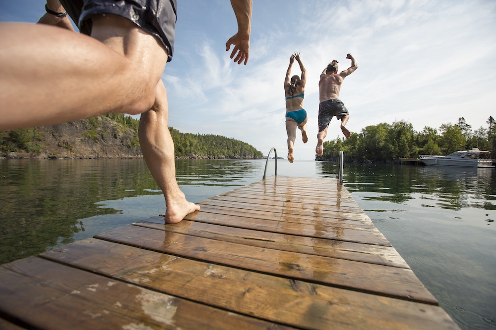 Three people running and jumping off a dock into the water