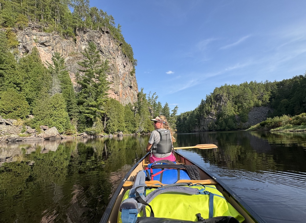 Woman in bow of canoe with cliff walls in background