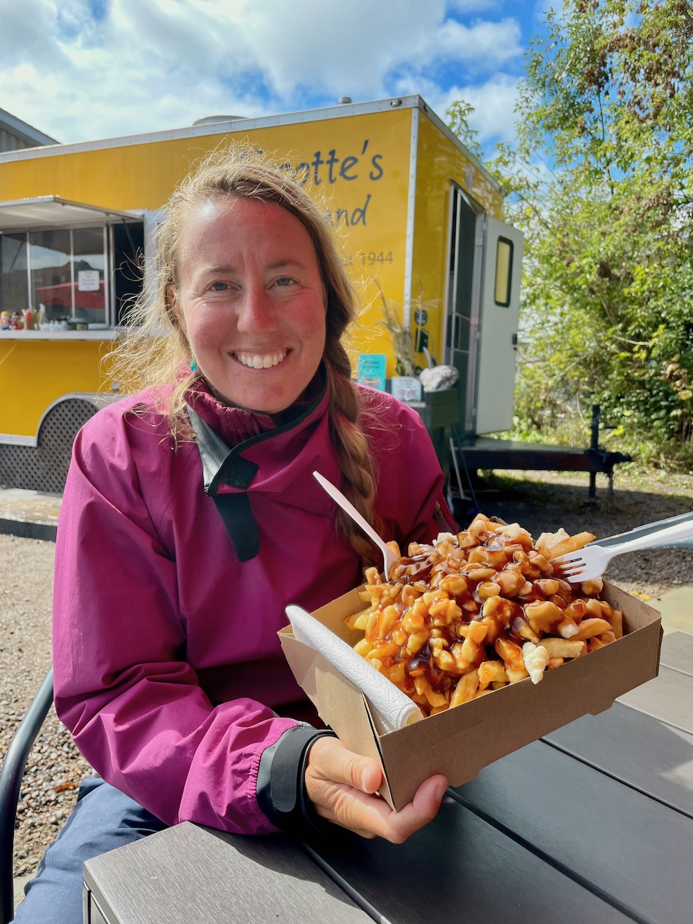 Woman sitting in front of chip truck holding a huge box of poutine.