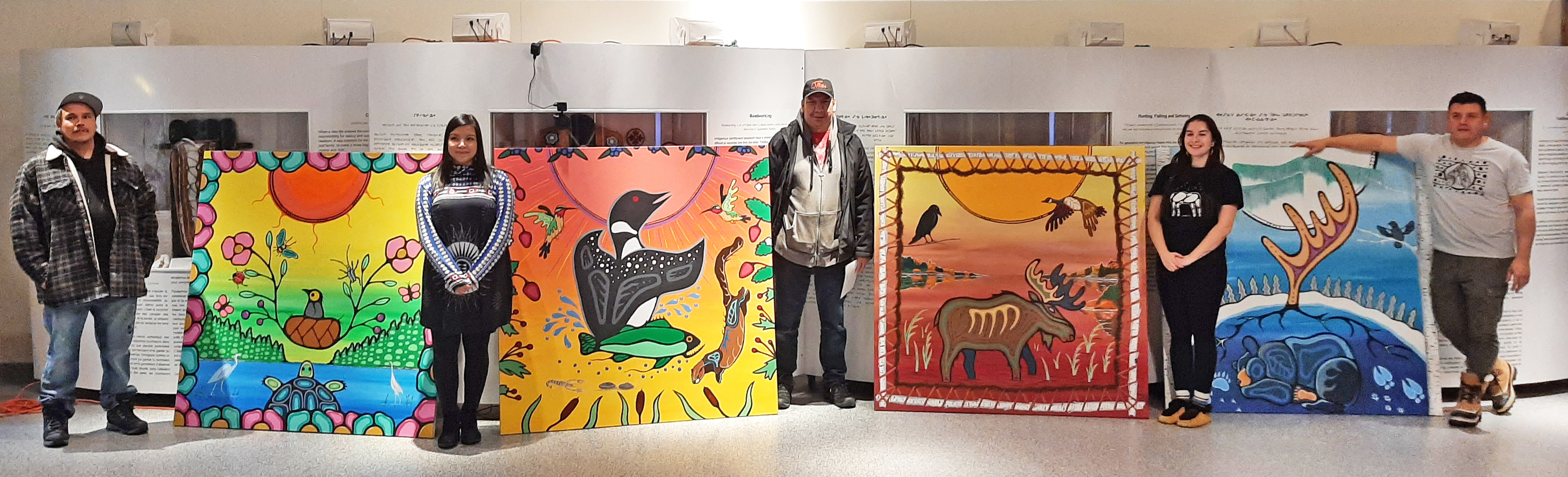 The five mural artists — Patrick Hunter, Storm Angeconeb, Darwin Peters, Jacinda Brisson, and Monias Rae — proudly stand beside their completed panels.