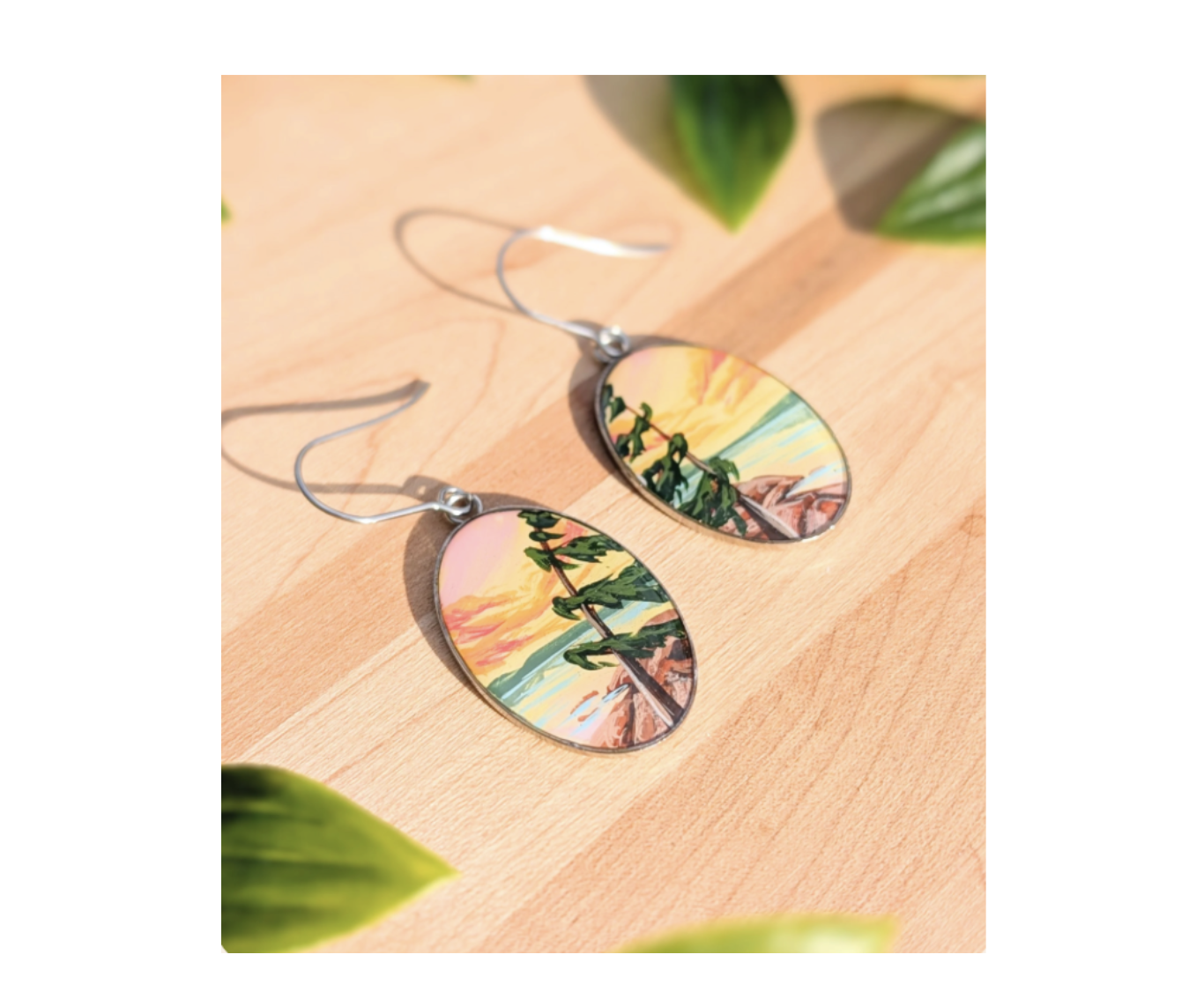 a pair of handpainted wooden earrings showing a windblown tree and delicate rose and orange sunset.