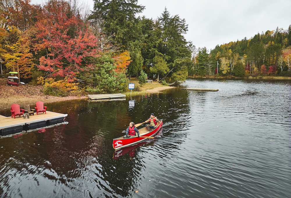 Two people paddle red canoe by a dock