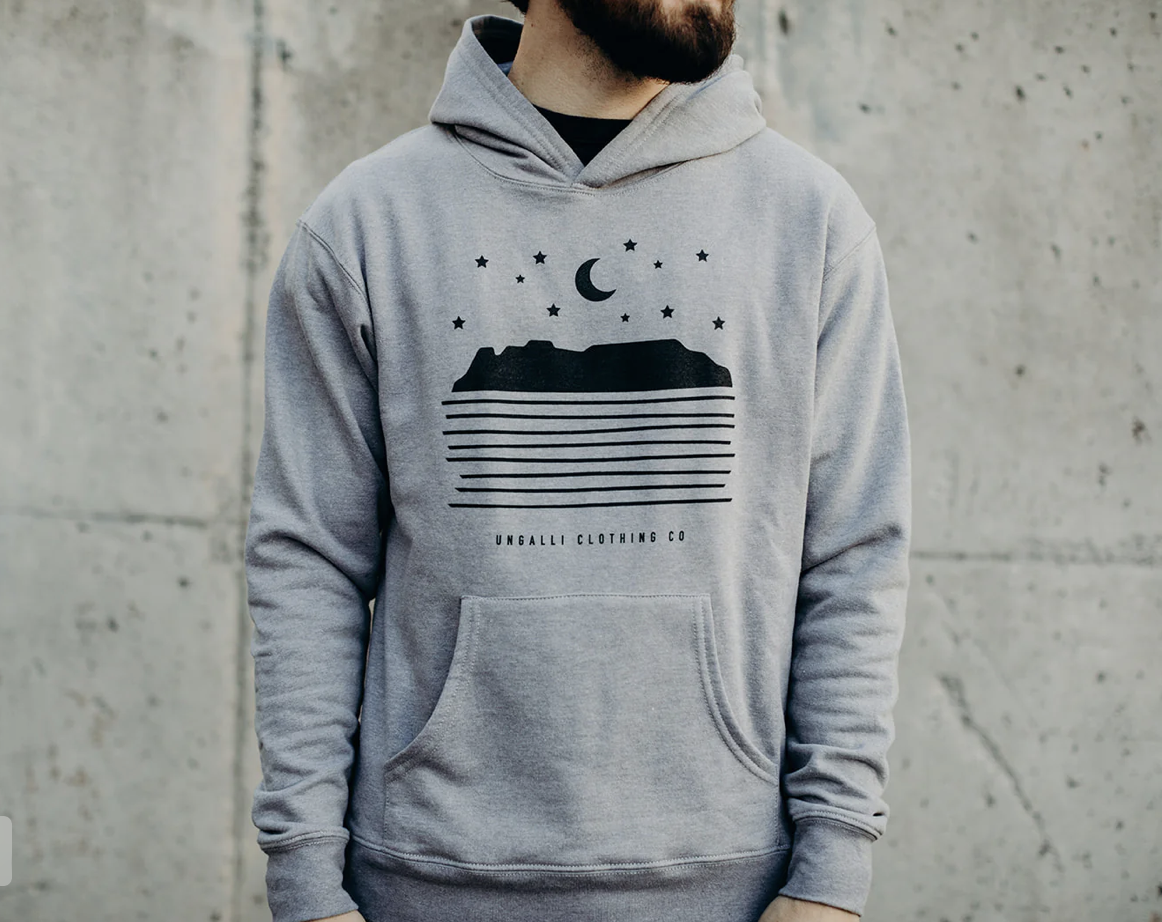 A grey hoodie printed with a stylized image of Sleeping Giant with waves of calm water in front of it and stars above, made in Thunder Bay Ontario.