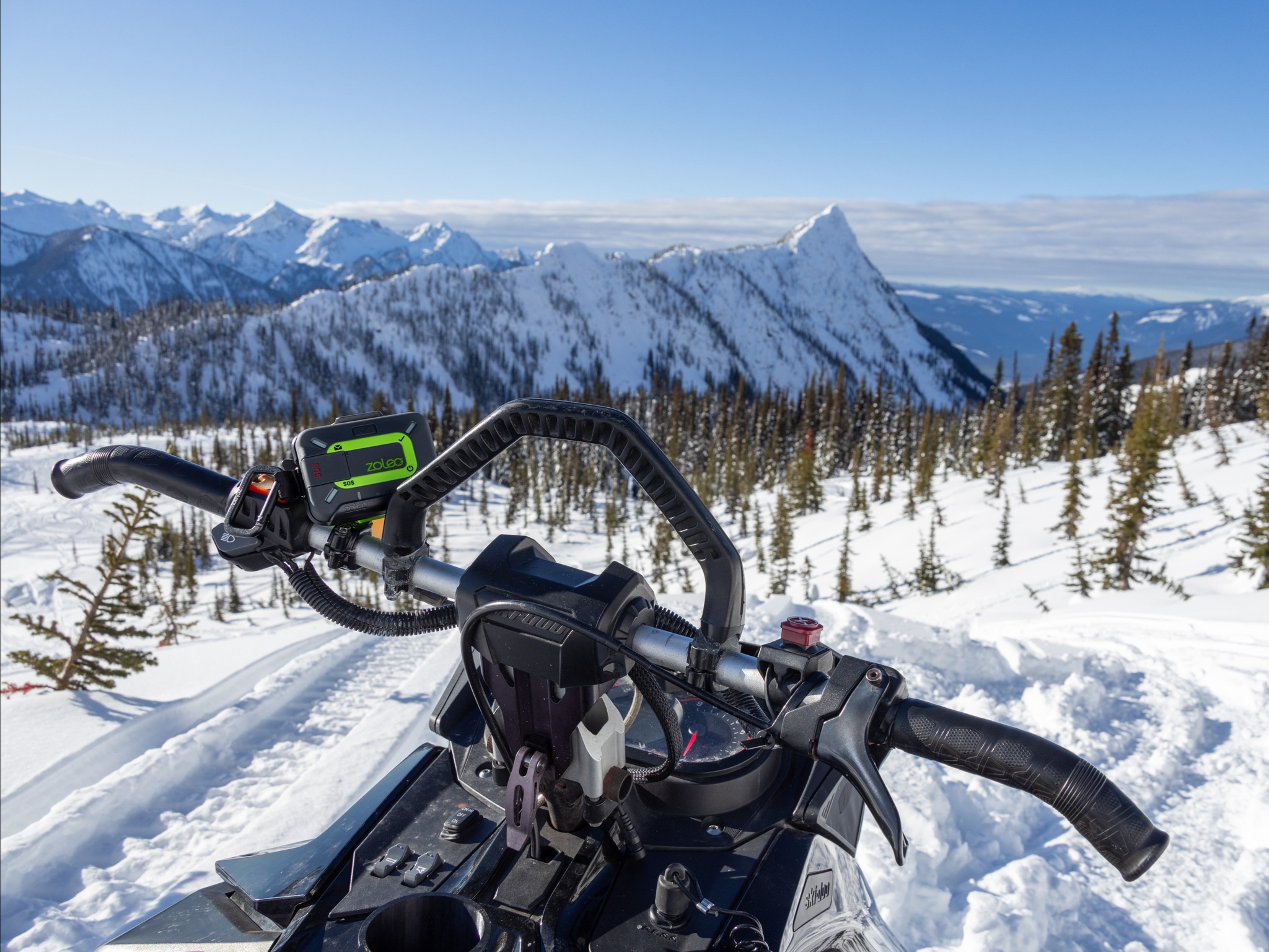 a snowmobile parked at the top of a snowy mountain with a ZOLEO satelite communication device on the handlebars.