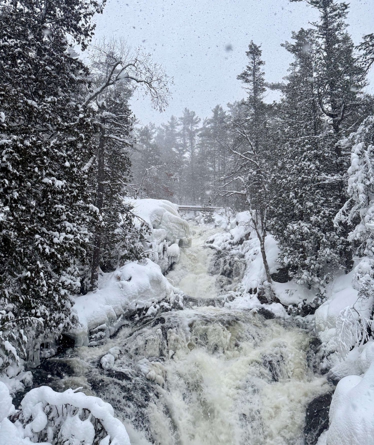 snow falls gently over a rushing Crystal Falls, surrounded by a snowcovered forest. 