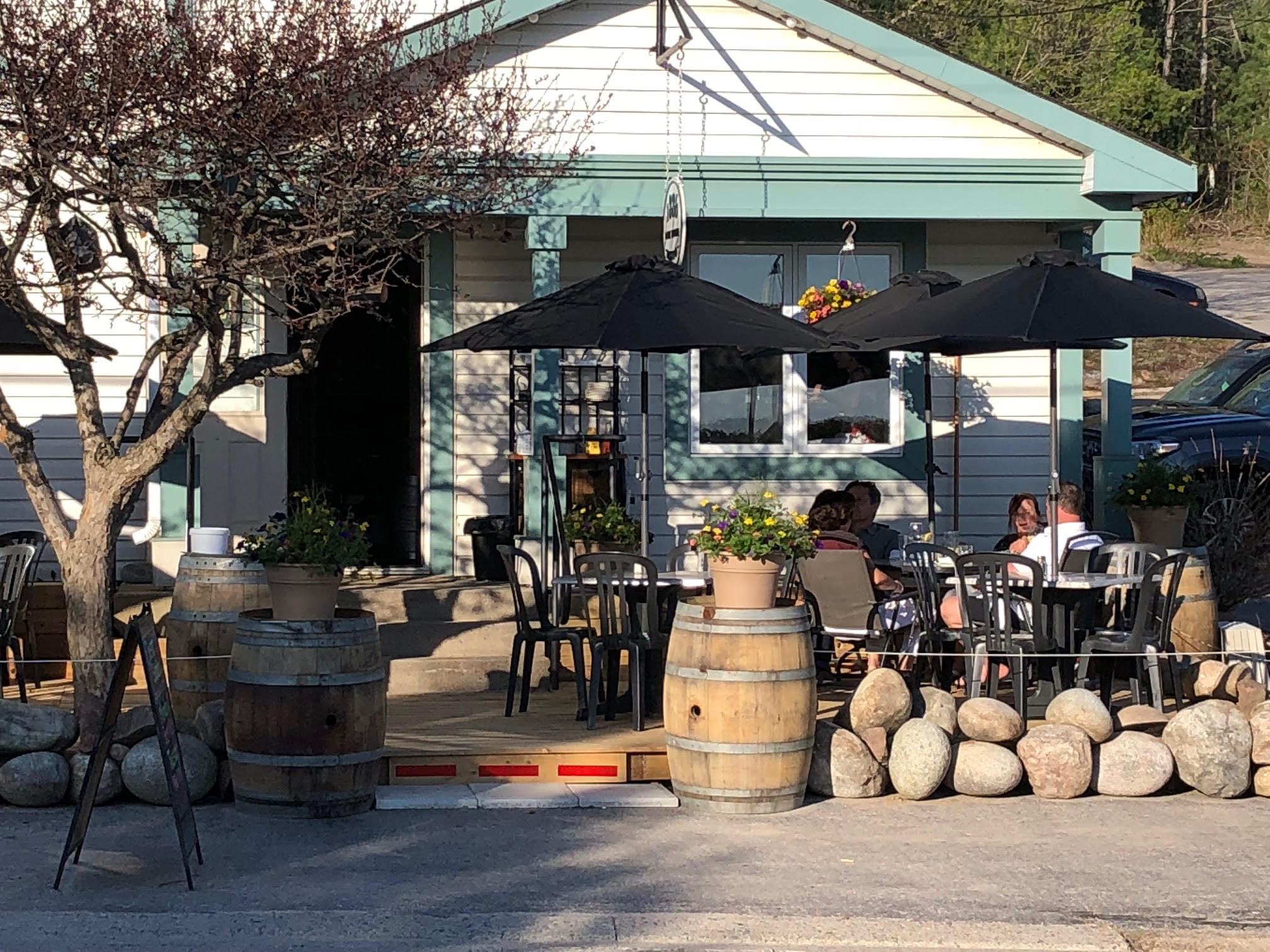 an inviting outdoor patio in front of 1886 Lakehouse in North Bay, with several outdoor tables with umbrellas and large wooden casks all around.