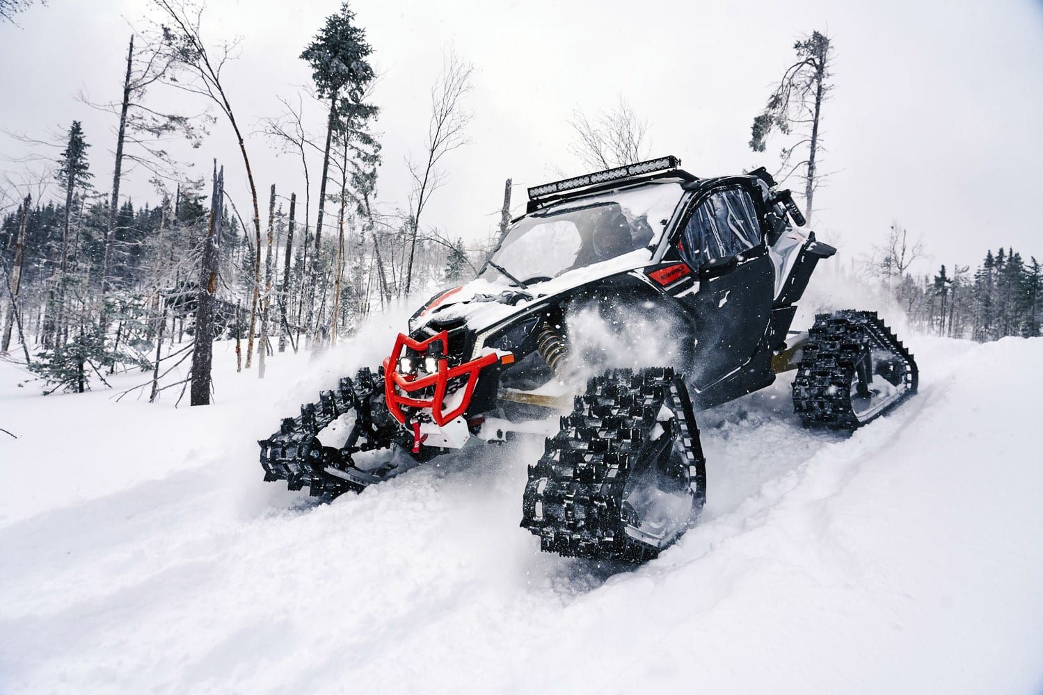 A red Can-Am Apache tracked ATV kicking up powder as it rolls through the snow on a winter day.