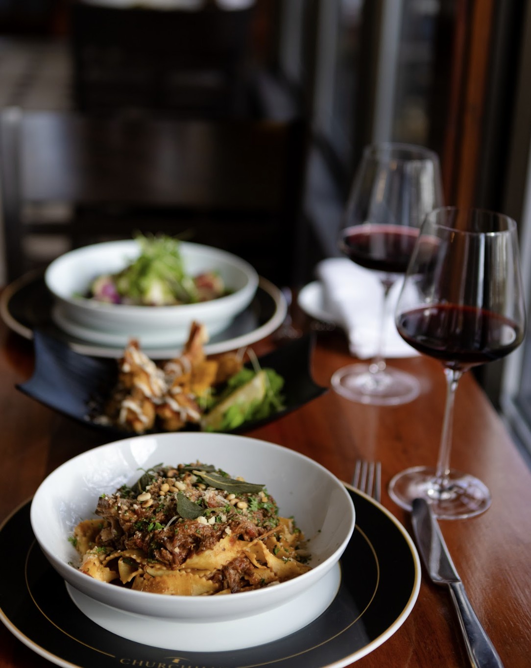 two elegantly plated entrees with and glasses of wine on a dining table at Churchill's North Bay.
