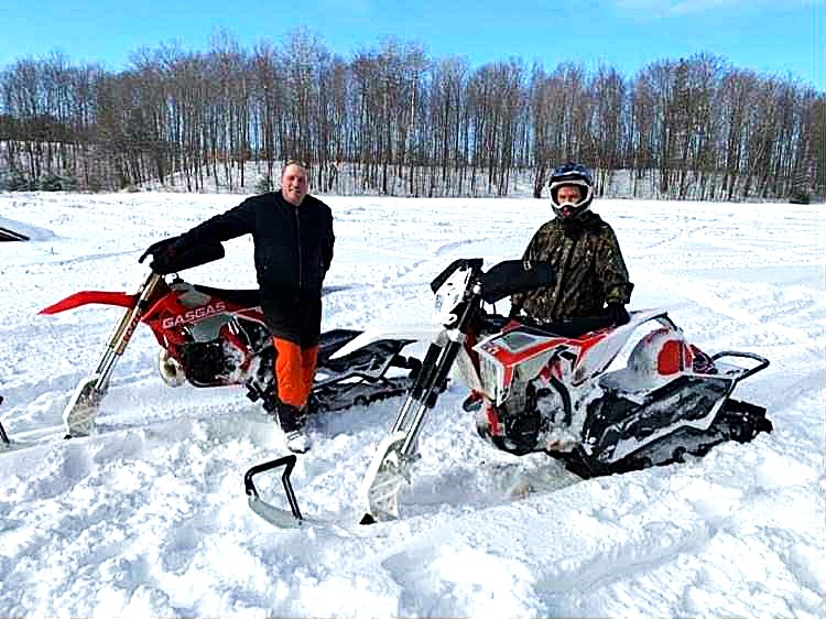 two people smiling sitting on snowbikes on a snowcovered frozen lake surrounded by forest. 