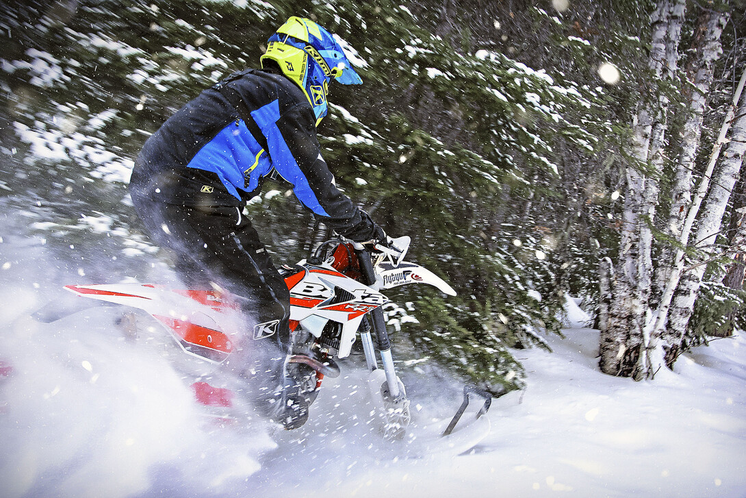 a rider on a snowbike flies through a cloud of powdered snow in a snowcovered forest.
