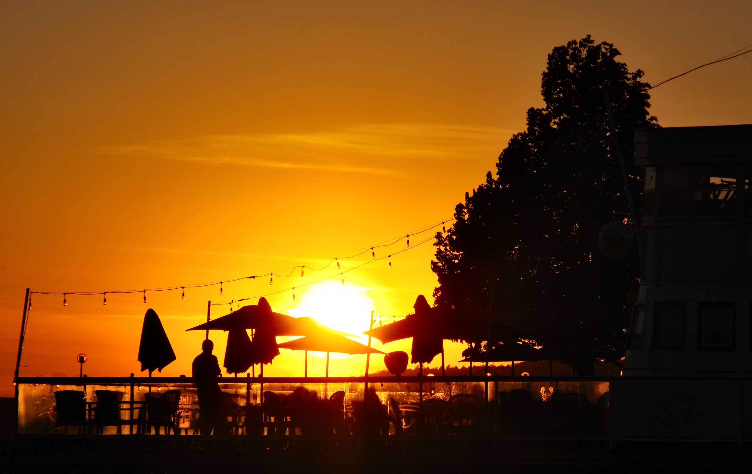 a bright golden sunset over patio tables and umbrellas next to the lakeside in North Bay.
